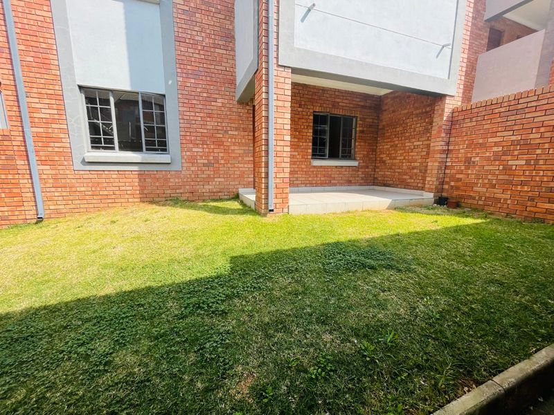 A private rear garden area featuring a small tiled patio, brick exterior walls, and security-fitted windows.