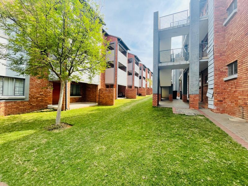 Exterior view of an apartment complex featuring face brick facades, private balconies, paved walkways, and a well-maintained communal lawn area.