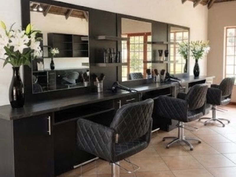 A professional salon space featuring built-in vanity stations with integrated mirrors, tiled flooring, and exposed timber rafters.