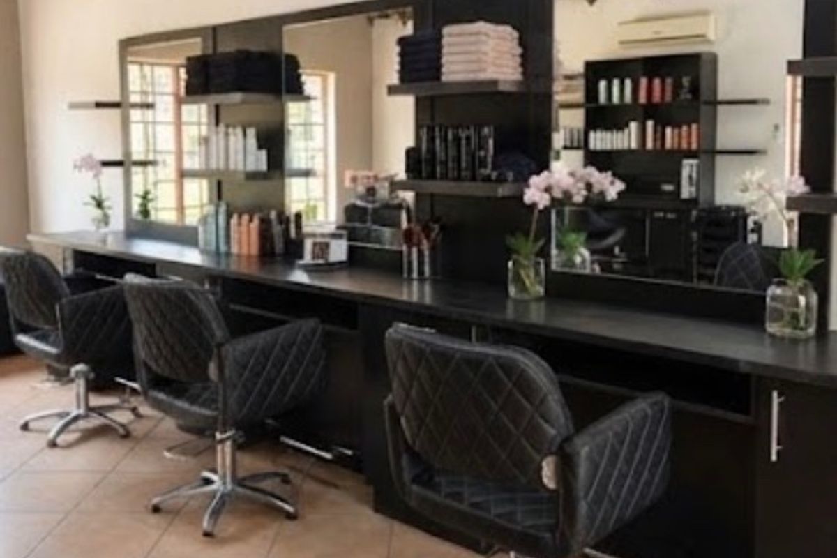 A professional salon workspace featuring multiple built-in vanity stations with large mirrors, integrated shelving, and tiled flooring.