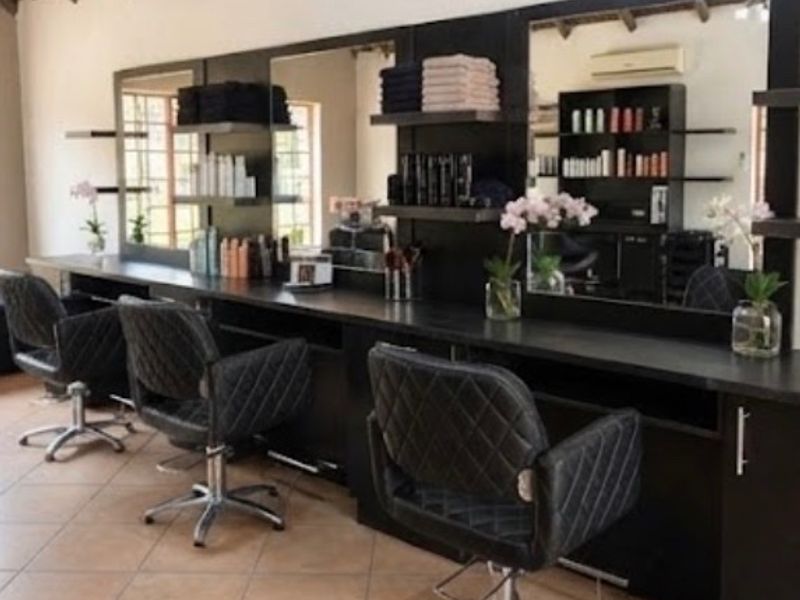 A professional salon workspace featuring multiple built-in vanity stations with large mirrors, integrated shelving, and tiled flooring.