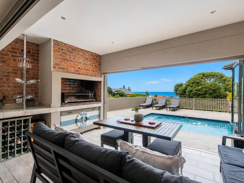 Covered patio featuring a built-in braai, exposed brickwork, and seamless flow to the pool deck with ocean views.