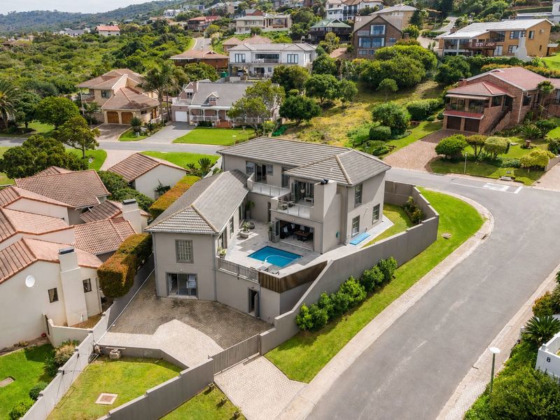 Aerial view of a modern multi-story residential property featuring a private swimming pool, paved driveway, and secure boundary walls in a suburban estate.