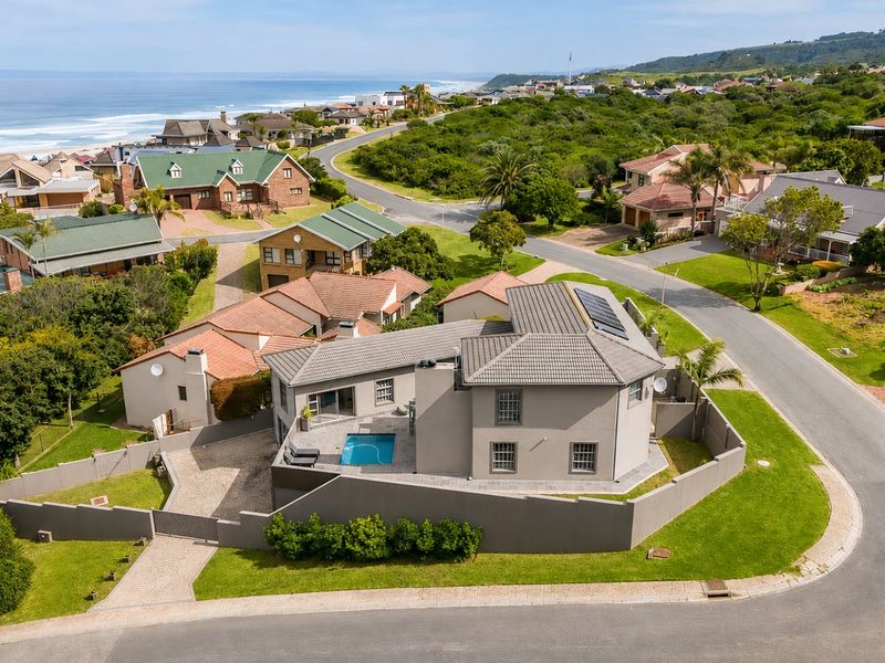 Aerial view of a coastal residential property featuring a swimming pool, solar panels, and a paved driveway within a landscaped estate setting.