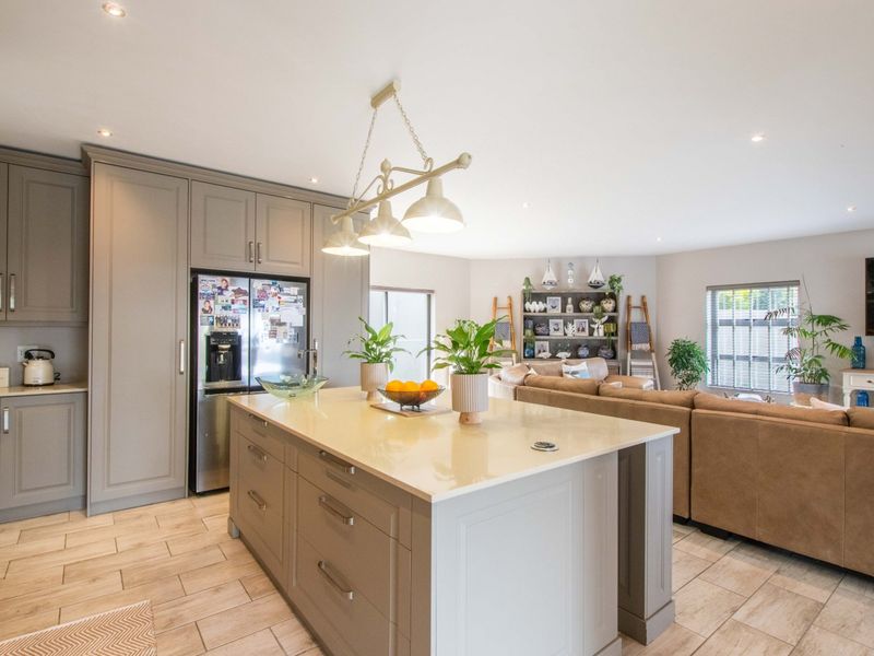 A modern open-plan kitchen and living area featuring a central island with quartz countertops, neutral cabinetry, and tiled flooring throughout.