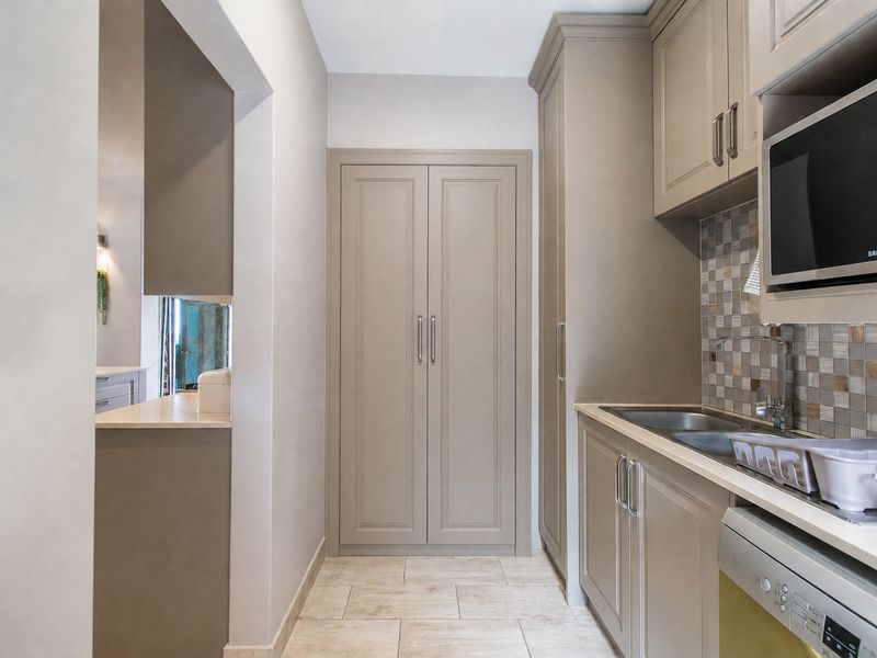 A well-maintained scullery featuring built-in cabinetry, a mosaic tile backsplash, stainless steel sink, and integrated microwave, offering efficient additional prep and storage space.