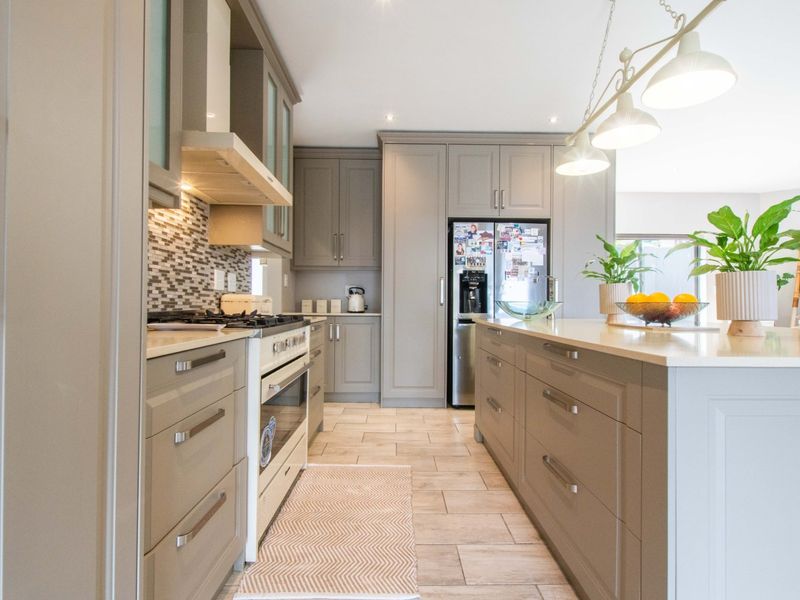 Modern kitchen featuring grey cabinetry, stone countertops, a central island, gas stove, and tiled flooring with integrated lighting.