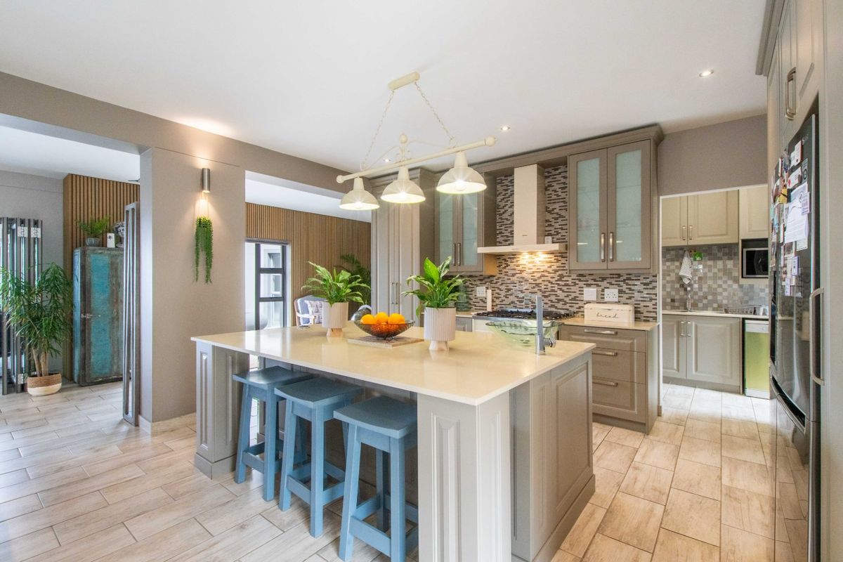 Modern kitchen featuring a central island with quartz countertops, ample built-in cabinetry, mosaic tile backsplash, and integrated lighting, with an adjacent scullery area.