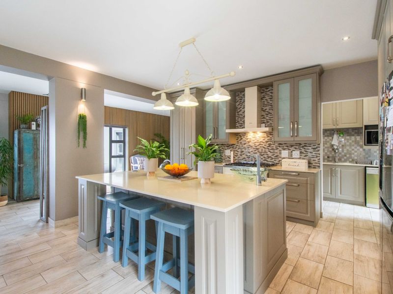 Modern kitchen featuring a central island with quartz countertops, ample built-in cabinetry, mosaic tile backsplash, and integrated lighting, with an adjacent scullery area.