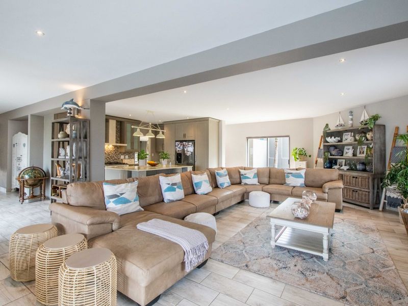 Spacious open-plan living area featuring a modern kitchen with a central island, neutral tiled flooring, and recessed lighting throughout the integrated space.