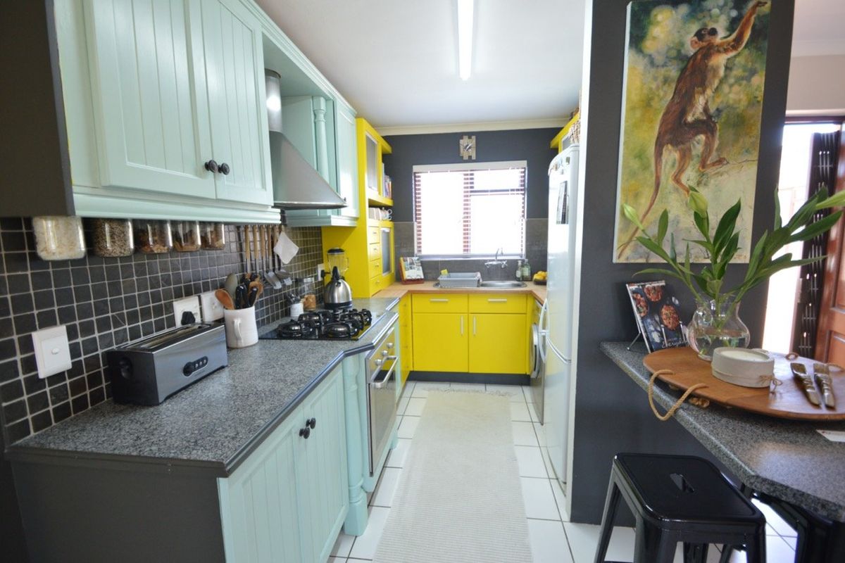 A compact kitchen featuring vibrant yellow and mint green cabinetry, granite countertops, a gas hob, and a tiled backsplash.