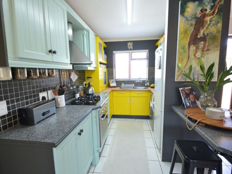 A compact kitchen featuring vibrant yellow and mint green cabinetry, granite countertops, a gas hob, and a tiled backsplash.