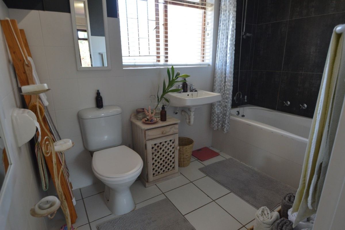 A functional bathroom featuring a wall-mounted basin, toilet, and a bathtub with shower fixtures, finished with neutral floor and wall tiling.
