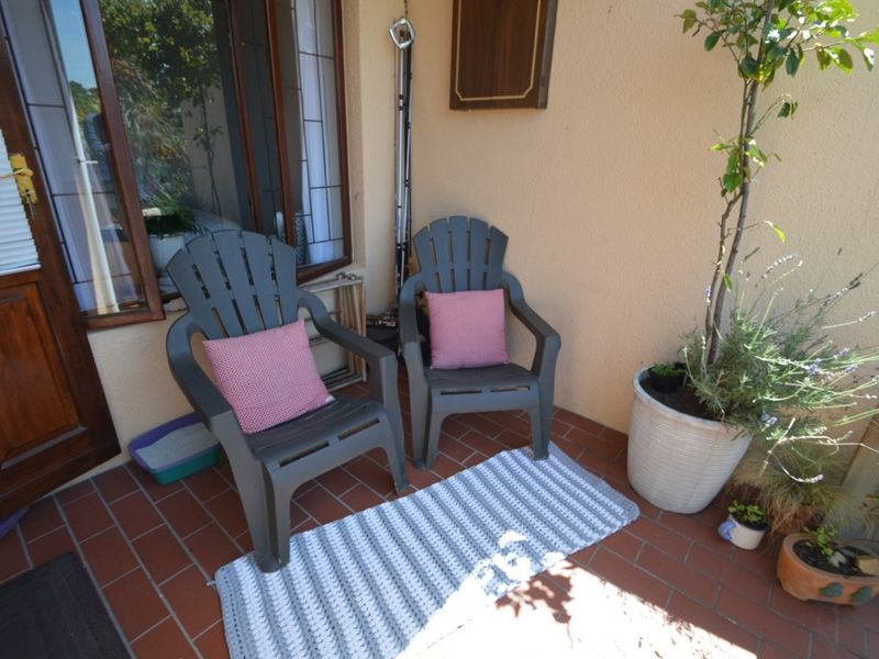A compact outdoor patio area featuring terracotta floor tiles and direct access to the interior through a timber-framed glass door.