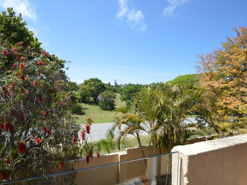 A scenic outdoor view overlooking a green landscape and street, featuring a modern glass balustrade and masonry wall.