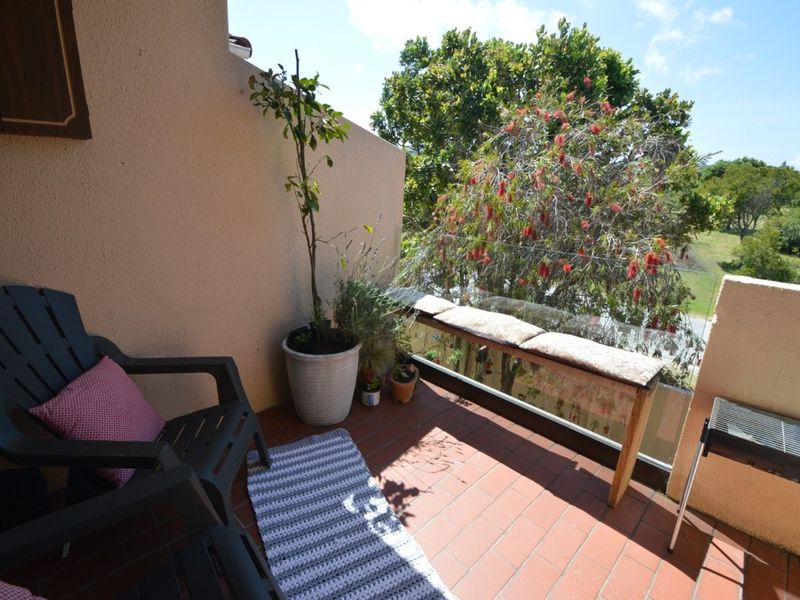 A private balcony featuring tiled flooring and a glass balustrade, offering an open outdoor space with views of surrounding greenery.