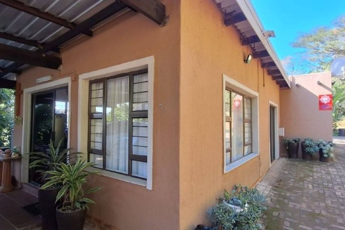 A view of the rear exterior of the townhouse, featuring a covered patio area with tiled flooring and a paved walkway along the side.
