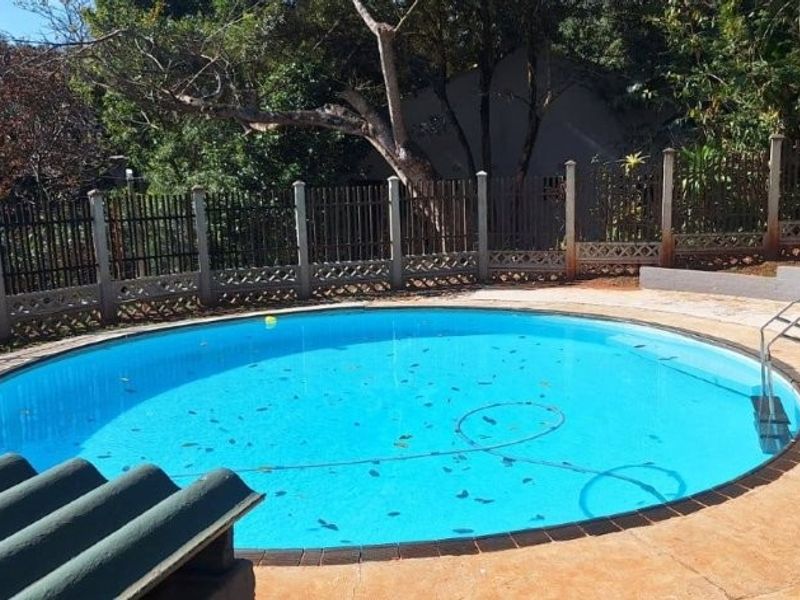 A circular swimming pool featuring a metal ladder and paved surround, enclosed by perimeter fencing with surrounding garden greenery.