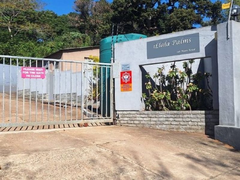 The entrance to the Ilala Palms townhouse complex, featuring a secure gated access point, concrete driveway, and perimeter boundary wall with electric fencing.