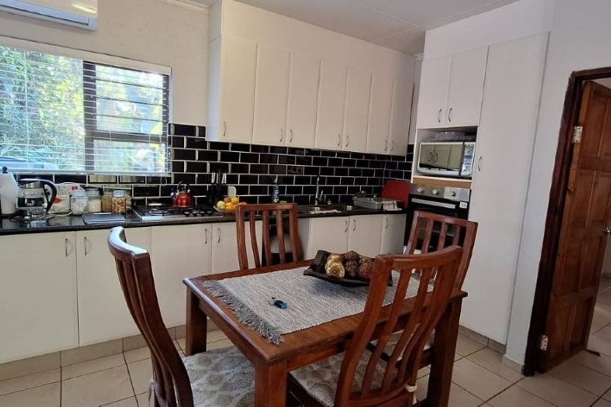 A functional kitchen featuring white cabinetry, black subway tile backsplash, granite countertops, and integrated appliances, with an adjacent dining area.