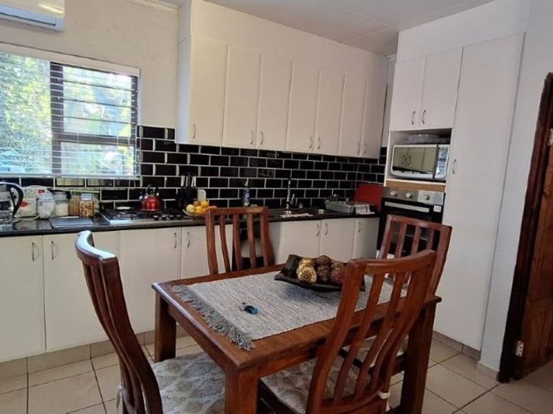 A functional kitchen featuring white cabinetry, black subway tile backsplash, granite countertops, and integrated appliances, with an adjacent dining area.