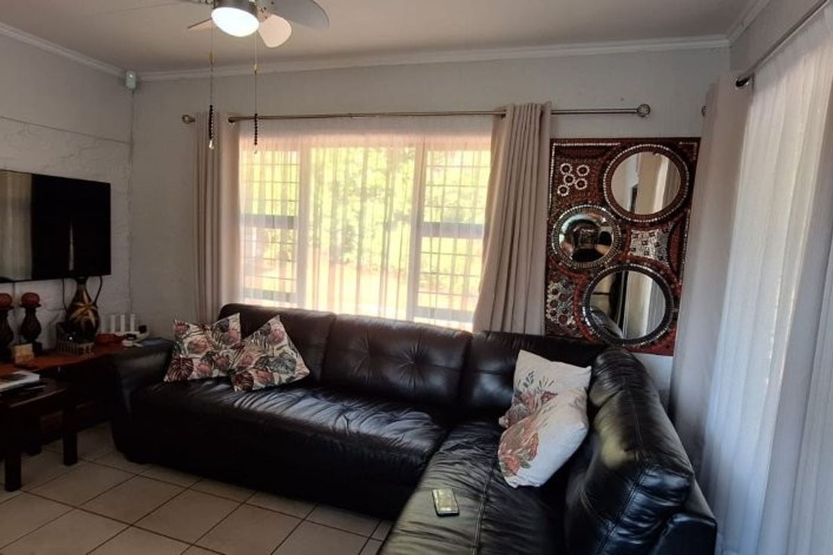 A living room featuring tiled flooring, a ceiling fan, and large windows fitted with security bars.