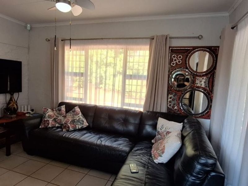 A living room featuring tiled flooring, a ceiling fan, and large windows fitted with security bars.