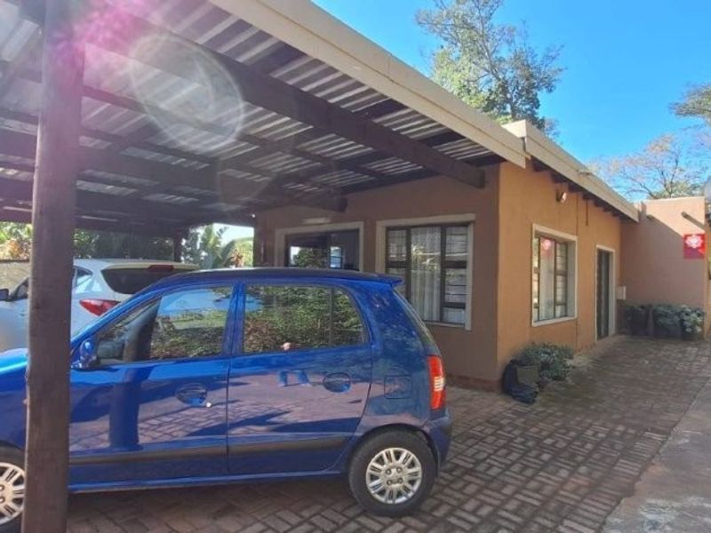 Front exterior view of the townhouse featuring a covered carport with timber supports and a paved driveway area.