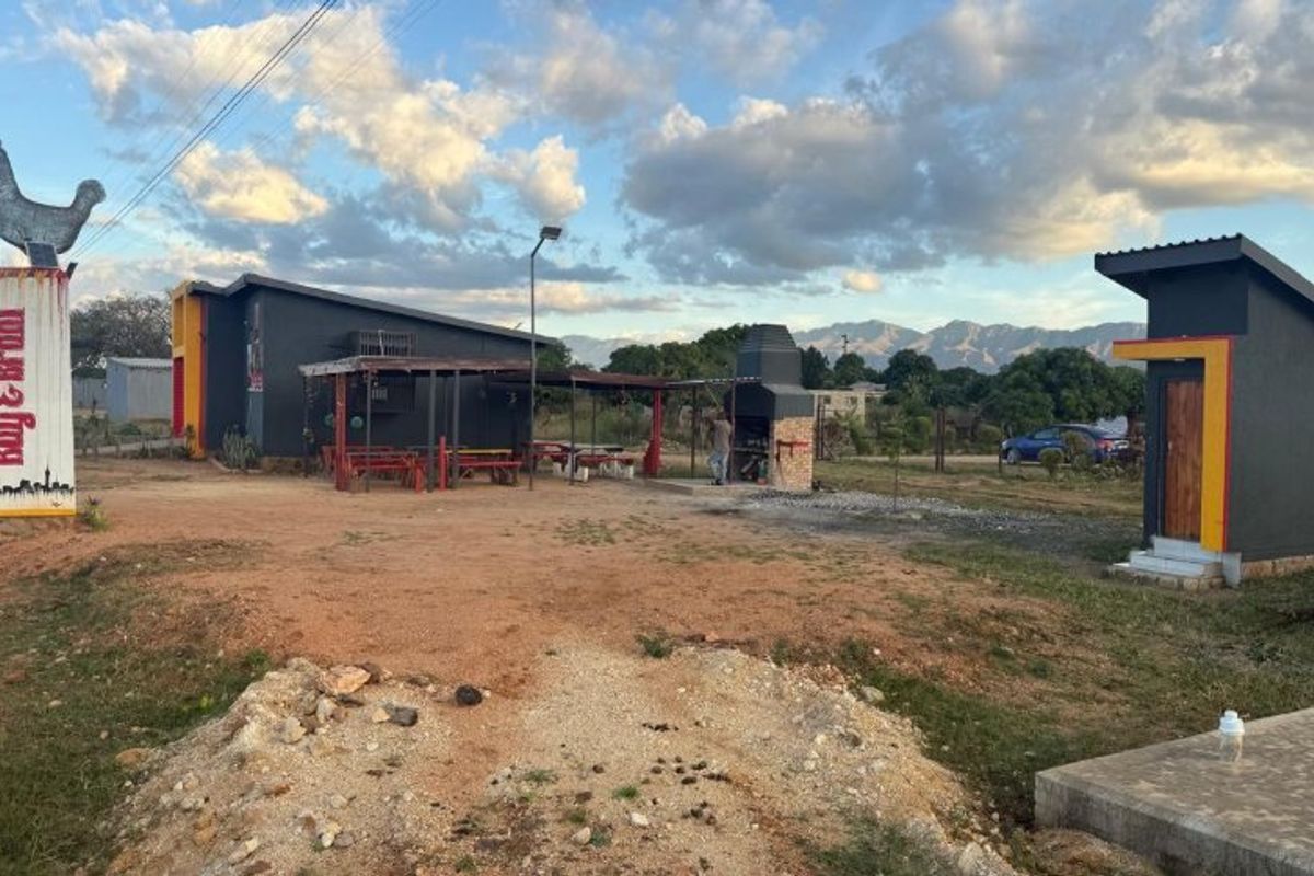 Commercial property exterior featuring a built-in braai area, covered patio space, and prominent signage, set against a mountain backdrop.