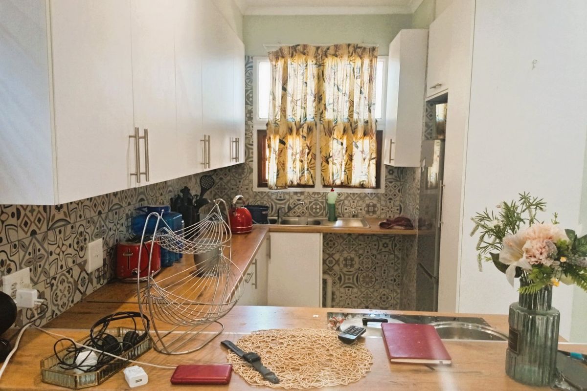A functional kitchen featuring white cabinetry, wooden countertops, and a decorative patterned tile backsplash with integrated sink and recessed lighting.