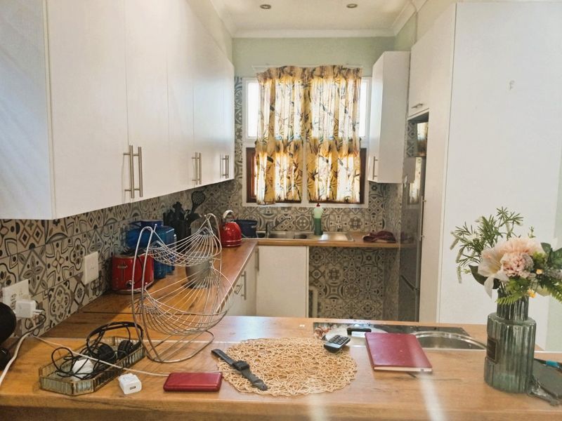 A functional kitchen featuring white cabinetry, wooden countertops, and a decorative patterned tile backsplash with integrated sink and recessed lighting.