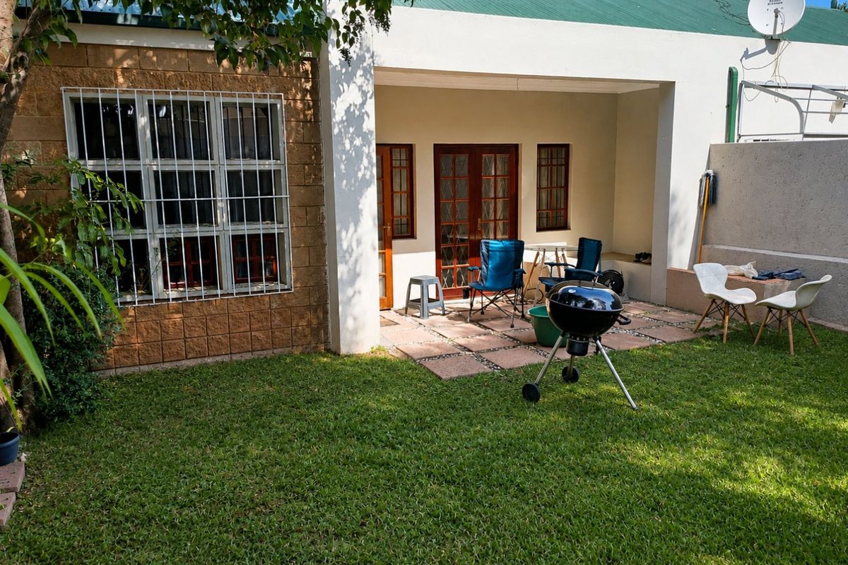 A rear view of the apartment featuring a covered patio area, paved flooring, and a private garden space.
