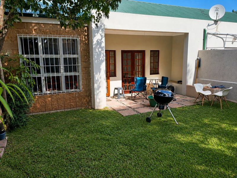 A rear view of the apartment featuring a covered patio area, paved flooring, and a private garden space.