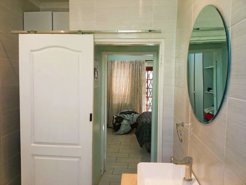 A functional bathroom featuring a wall-mounted basin with chrome fixtures and a sliding door, providing access to the adjacent bedroom area.