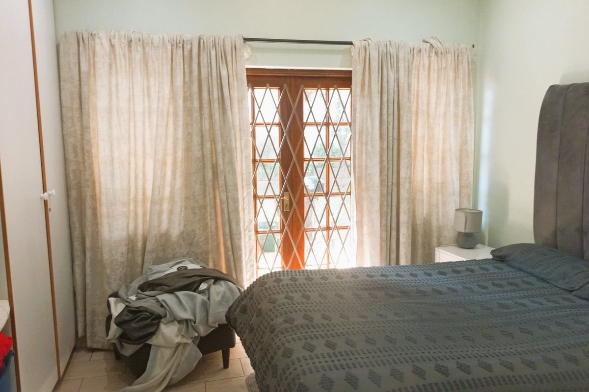 A bedroom featuring tiled flooring, a built-in wardrobe, and wooden french doors with a security gate providing access to the exterior.