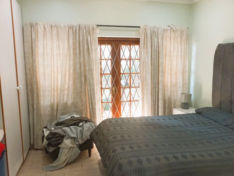 A bedroom featuring tiled flooring, a built-in wardrobe, and wooden french doors with a security gate providing access to the exterior.