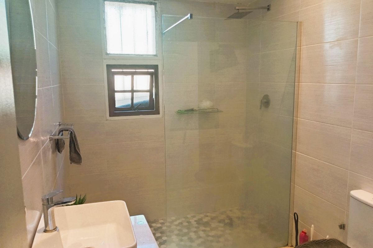 Modern bathroom featuring a glass-enclosed walk-in shower with a rain shower head, vessel sink, and neutral wall tiling.