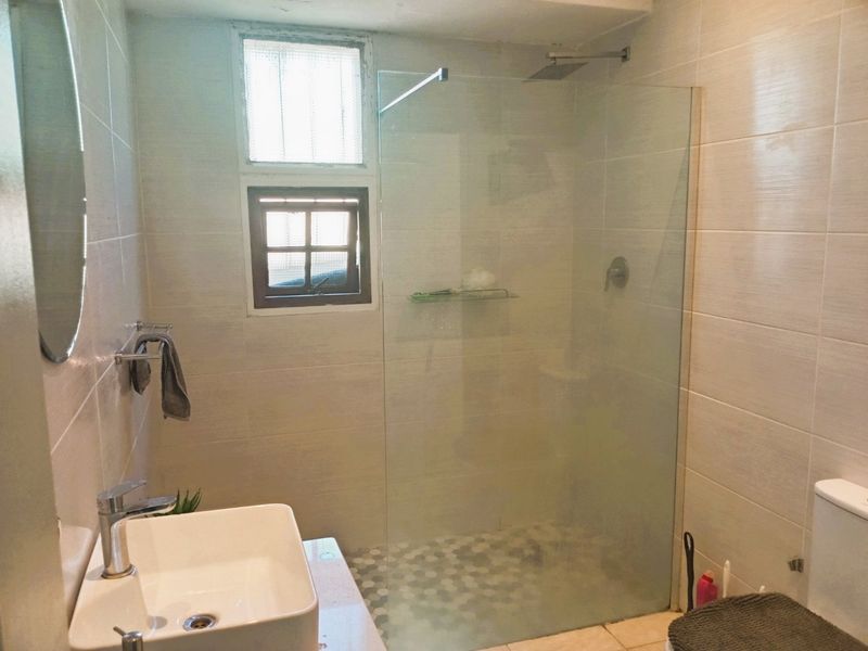 Modern bathroom featuring a glass-enclosed walk-in shower with a rain shower head, vessel sink, and neutral wall tiling.