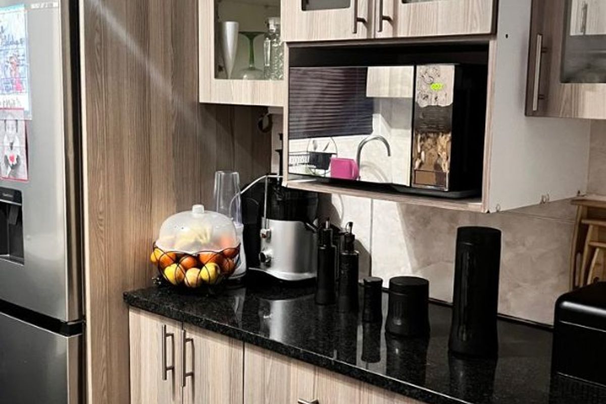 A modern kitchen featuring wood-grain laminate cabinetry, sleek granite countertops, and built-in microwave housing with glass-front upper storage units.