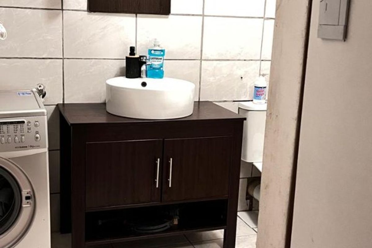 A functional bathroom featuring a dark wood vanity with a vessel sink, tiled walls and flooring, and a dedicated space for a washing machine.