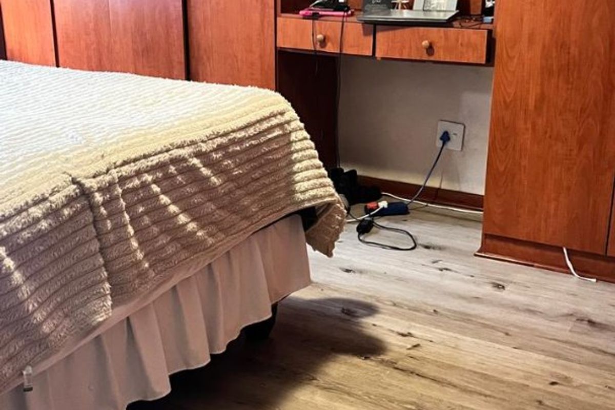 Bedroom featuring wood-finish built-in cupboards with an integrated vanity unit and modern light-toned laminate flooring.