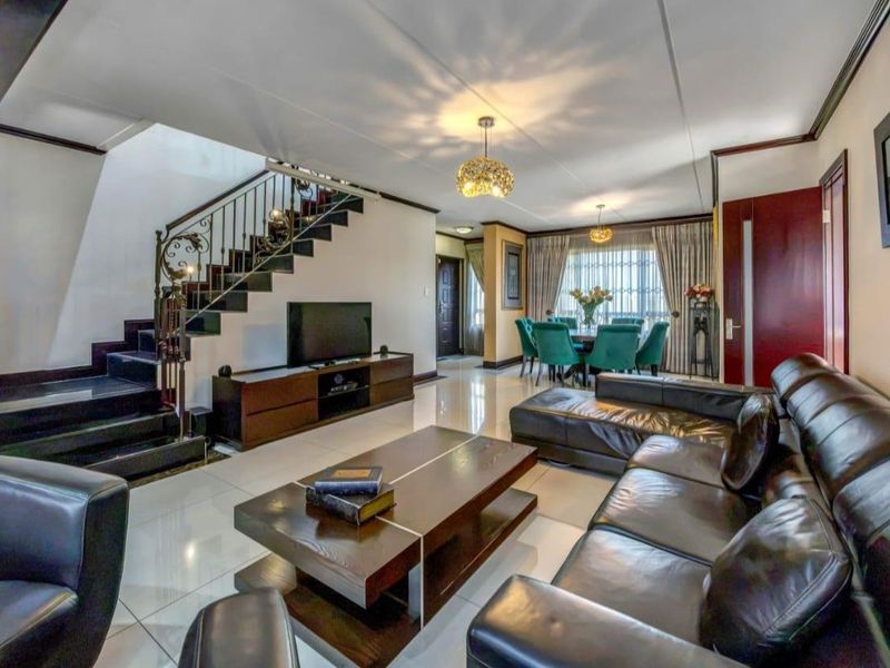Spacious open-plan living and dining area featuring polished tiled floors, a striking staircase with wrought iron detailing, and integrated lighting.