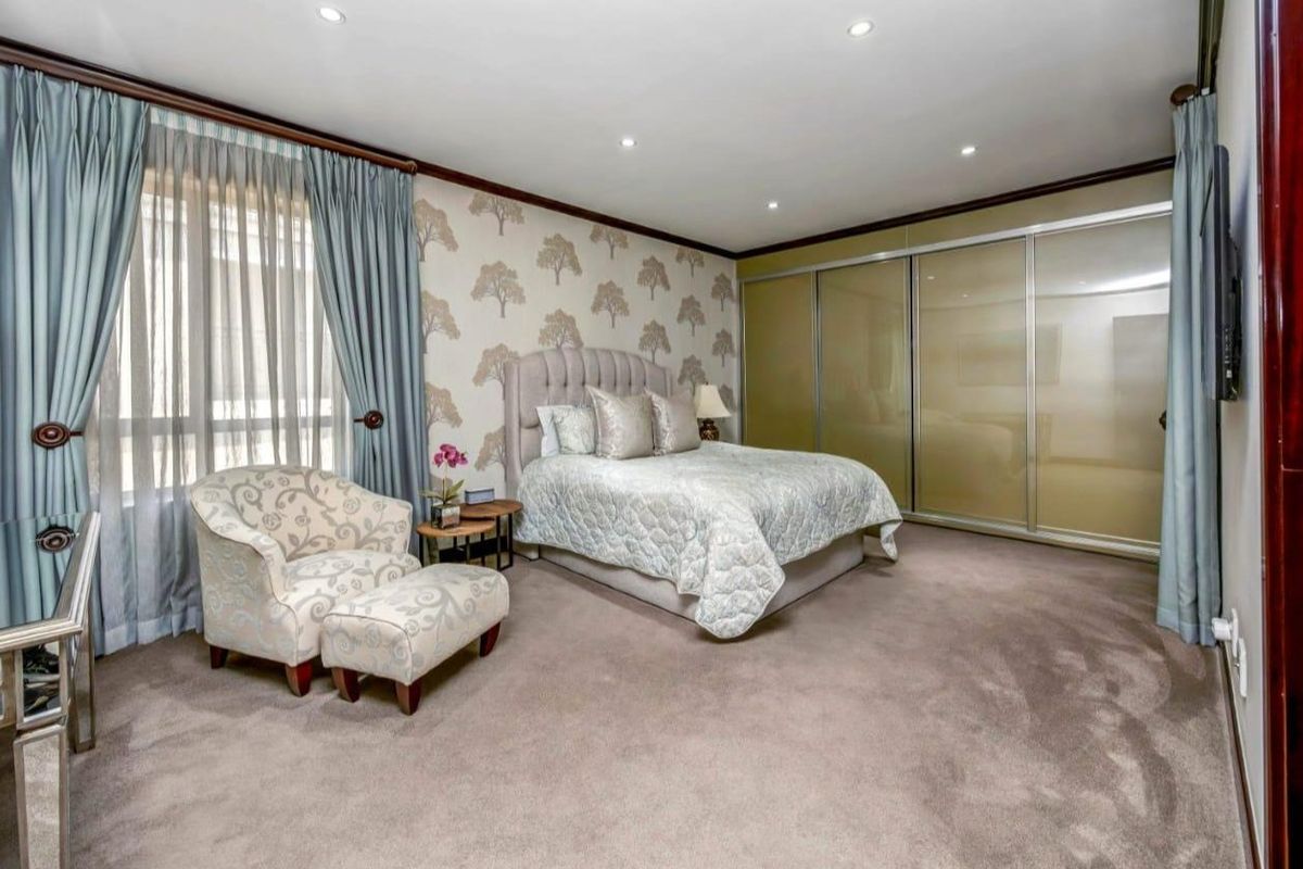 Spacious bedroom featuring neutral patterned wallpaper, recessed downlighting, plush carpeting, and large built-in sliding door wardrobes.