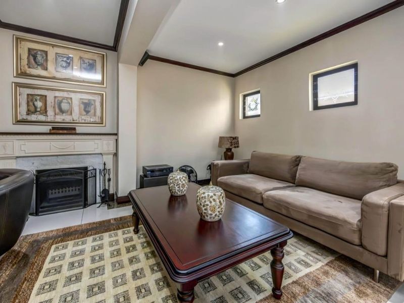 A comfortable living room featuring a classic fireplace with a mantelpiece, recessed lighting, and crown molding, finished with neutral tiled flooring.