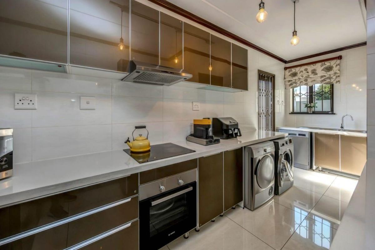 Modern kitchen featuring high-gloss cabinetry, stone countertops, integrated oven and hob, and tiled flooring with a dedicated laundry area.