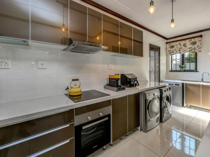 Modern kitchen featuring high-gloss cabinetry, stone countertops, integrated oven and hob, and tiled flooring with a dedicated laundry area.