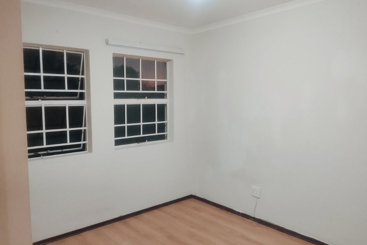 A clean, empty bedroom featuring laminate flooring, white walls, and windows fitted with security bars.