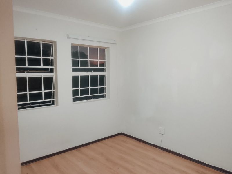 A clean, empty bedroom featuring laminate flooring, white walls, and windows fitted with security bars.