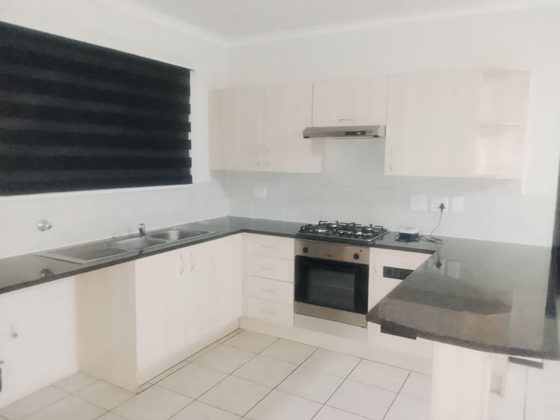 A clean, functional kitchen featuring light-toned cabinetry, dark granite countertops, a gas hob, built-in oven, and tiled flooring.