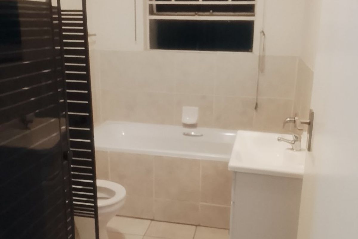 A functional bathroom featuring a bathtub, shower enclosure, vanity basin, and toilet with neutral tiled finishes.